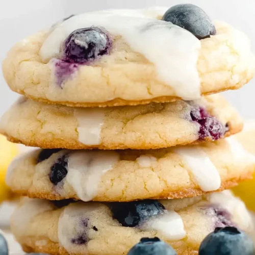 A stack of golden brown lemon blueberry cookies with a lemon glaze drizzle.