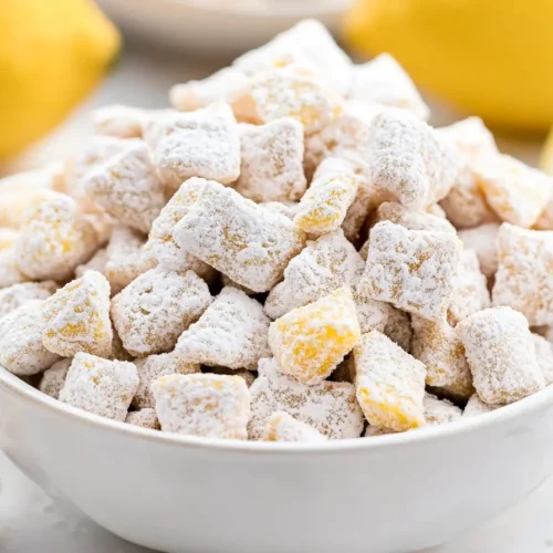 A bowl of lemon puppy chow with powdered sugar and lemon slices.